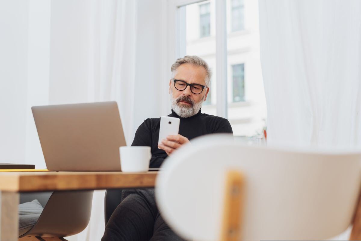 Mann bei Workation auf dem Stuhl sitzend und aufs Handy schauend